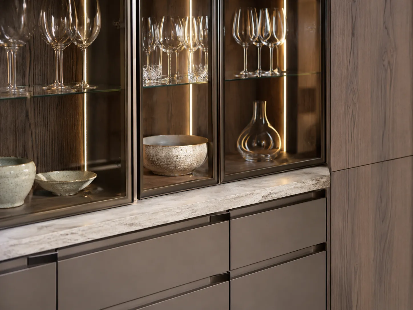 Sideboard cabinet detail with glass doors, warm LED lighting, closed drawers, and displayed glassware.