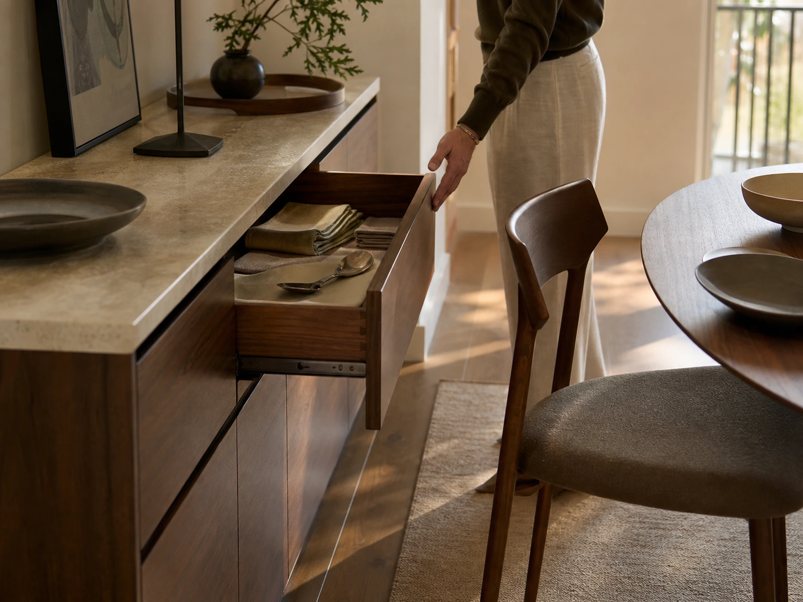 Open sideboard drawer beside a pulled-out dining chair with usable passage remaining.