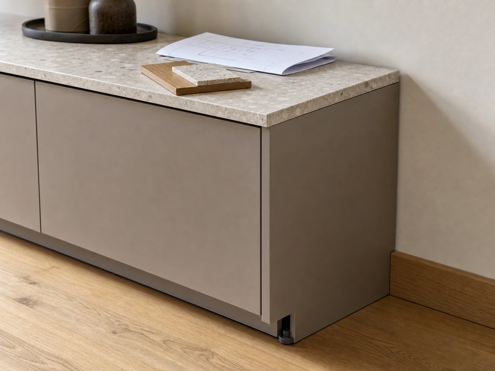 Stone sideboard edge, cabinet side, skirting junction, wall line, and material sample prepared for design review.